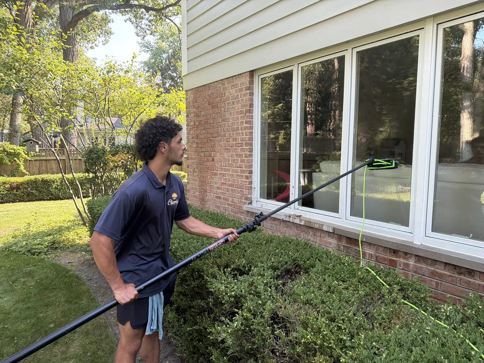 ClearDay technician cleaning exterior windows with a water-fed pole on a brick house