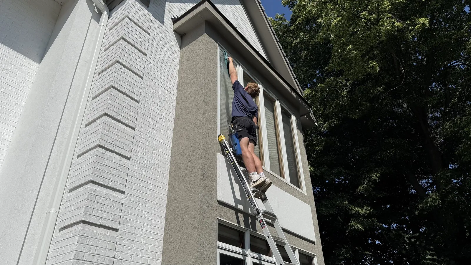 ClearDay technician detailing exterior windows from a ladder on a white house