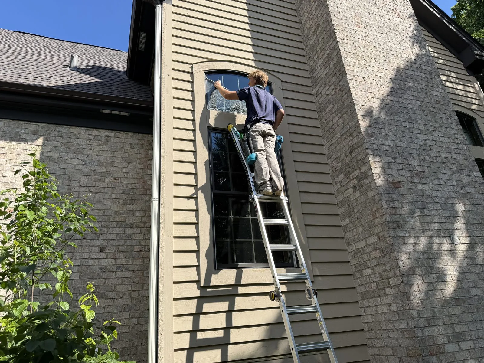 ClearDay technician cleaning exterior windows by hand from a ladder