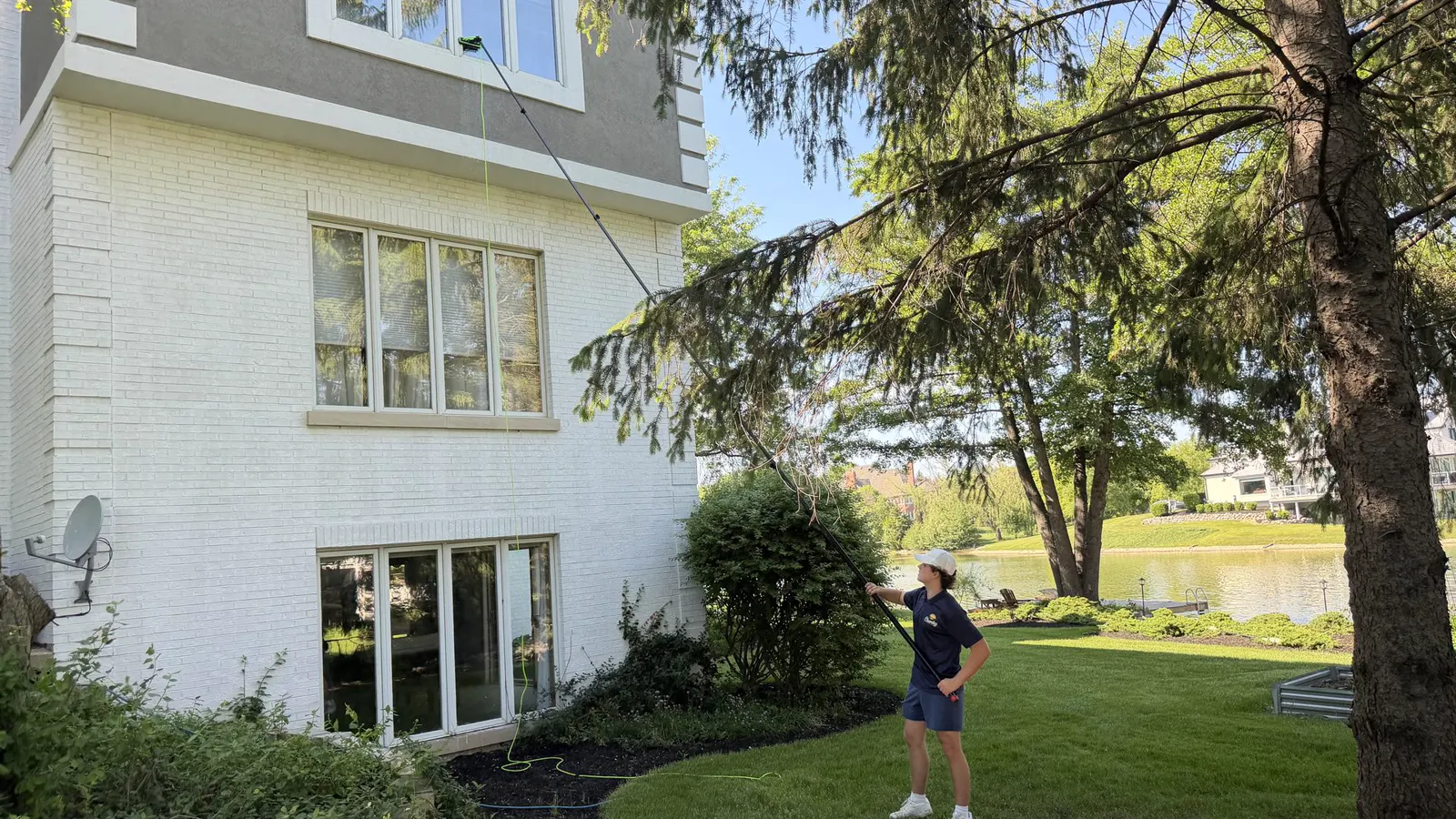 ClearDay technician cleaning exterior windows with a water-fed pole on a white lakeside house