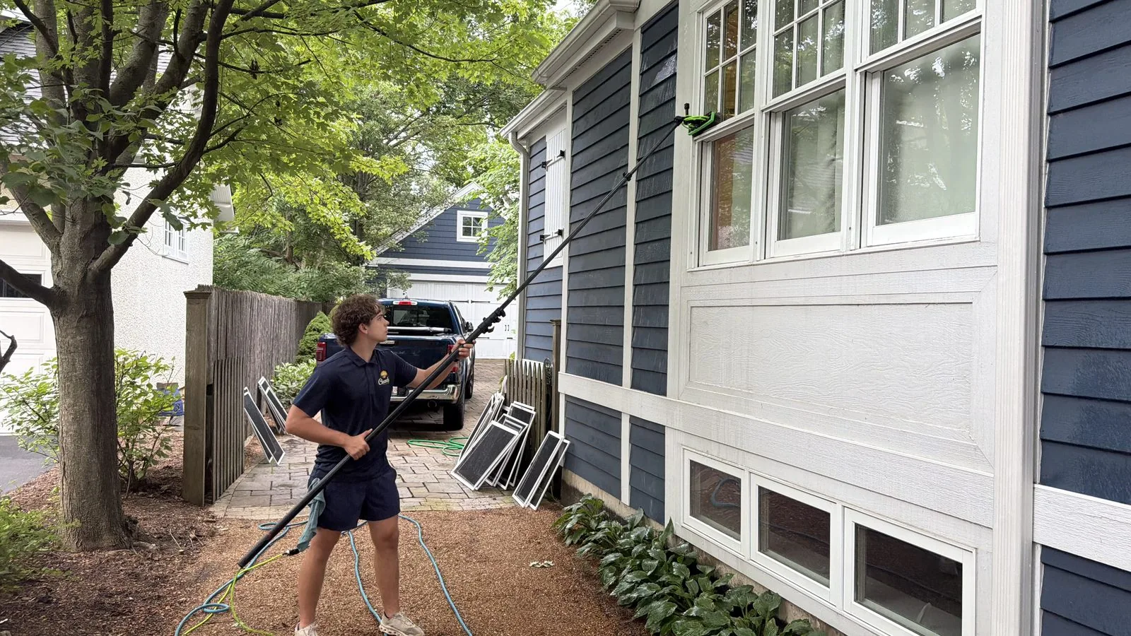 ClearDay technician cleaning exterior windows with a water-fed pole on a blue house